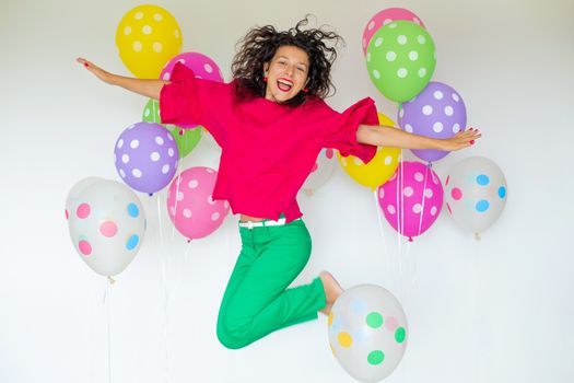 Young brunette girl posing in a jump with colorful balloons on a white background.