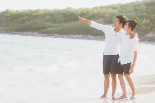 Homosexual portrait young asian couple standing pointing something together on beach in summer, asia gay going sea for leisure with romantic and happy in vacation at sea, LGBT with legal concept.