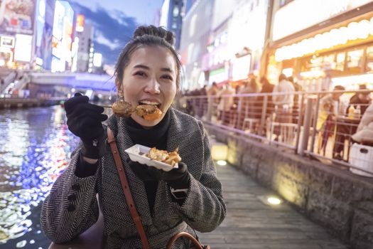 Young woman tourists enjoy eating street food in walking at street shopping center Dotonbori in Osaka, Japan.