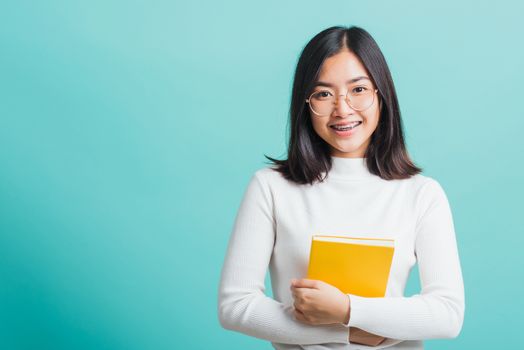 Portrait female in glasses is holding the books on hand, Young beautiful Asian woman hugging books, studio shot isolated on a blue background, Education concept