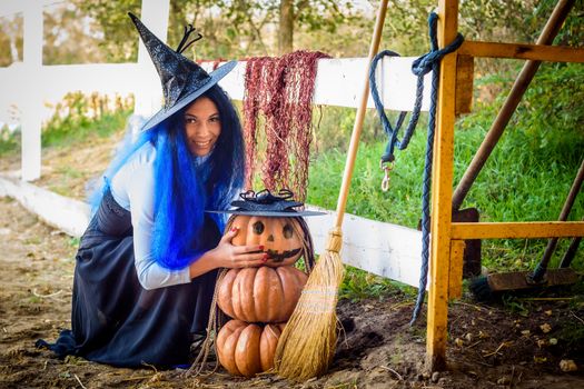 A girl in a witch costume, celebrating Halloween, sat down by a pumpkin with a drawn malicious grimace