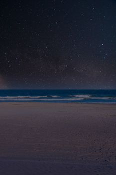 A Wide Open Beach Scene With a Man Walking Through the Scene With a Starry Night Sky in the Background
