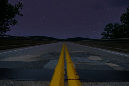A Low Angle Shot of a Road at Night With Trees on Each Side and Stars in the Sky