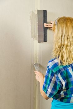 Woman working with spatula tool. Builder female indoor worker plastering wall with spatula tool. Woman putty plaster.