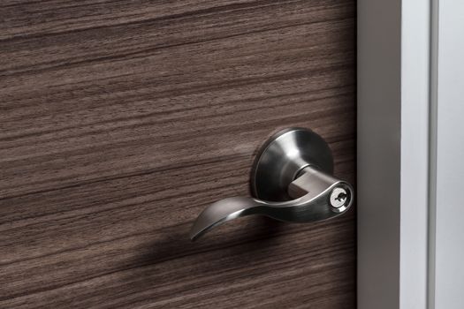 stainless steel door knob or handle with keyhole on wooden door, wave style lever handle front door knob with lock, modern interior design concept, shallow depth of field