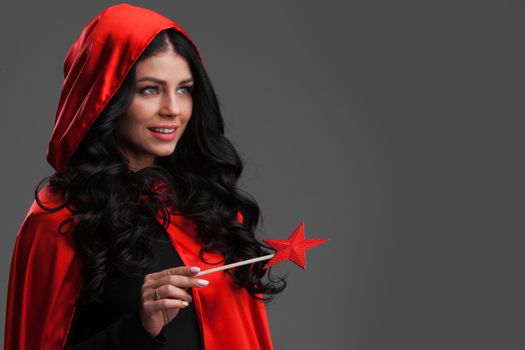 Woman in red cape with star shaped magic wand , gray background