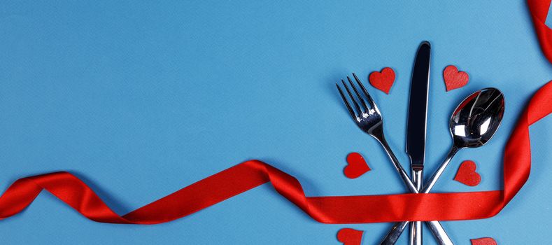 Cutlery set tied with red silk ribbon and hearts on blue background Valentine day dinner concept