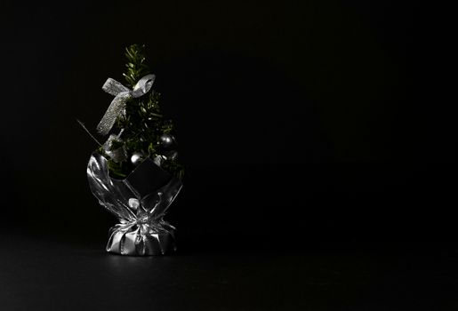 Small Christmas tree in a bag with decorations. Table accessory with silver decor. Christmas tree on black background for greeting cards