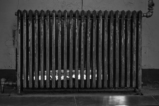 Vintage and retro or old-fashioned heating radiator against a wall. Worn-out and obsolete. Black and White processing.