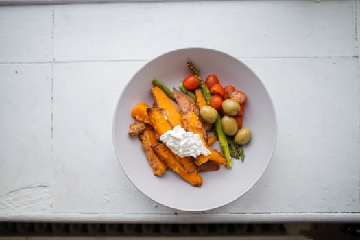 Sweet potato fries with cottage cheese on top, olives, tomatoes, and asparagus dish from above. Nutritious dish with vegetables on white plate. Balanced diet