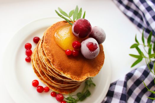 A stack of pancakes decorated with frozen cherries and cranberries on a white plate