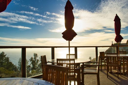 Wooden tables and chairs of a bar or restaurant terrace looking over the sea or ocean with moody and atmospheric sky in background.