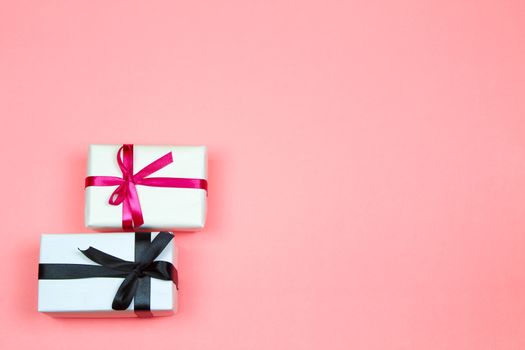 Gifts wrapped with white paper and pink and black bows on pink background