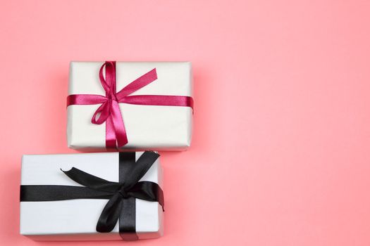 Gifts wrapped with white paper and pink and black bows on pink background