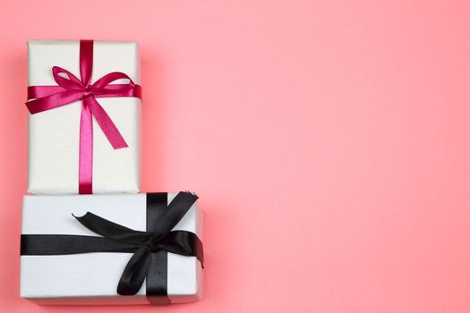 Gifts wrapped with white paper and pink and black bows on pink background