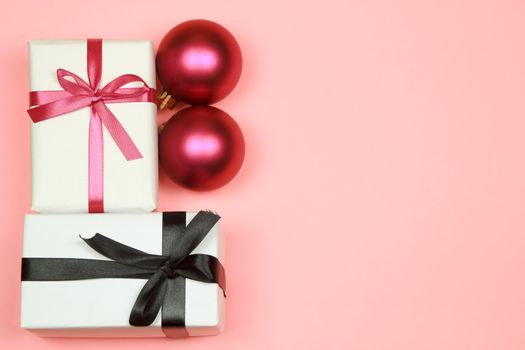 Gift wrapped with white paper and pink bow next to Christmas decoration on pink background