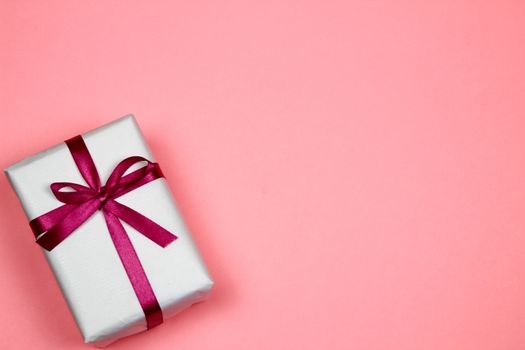 Gift wrapped with white paper and pink bow on pink background