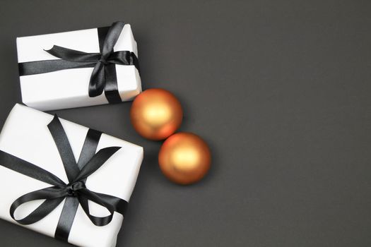 Gifts wrapped with white paper and black bows nex to Christmas decoration on black background