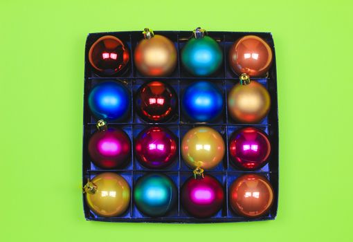 Box of multicolor Christmas balls on green background