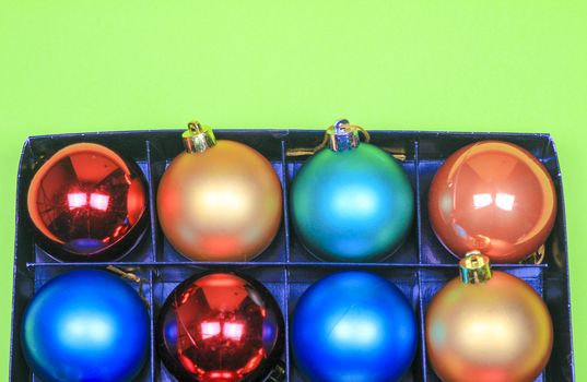 Box of multicolor Christmas balls on green background