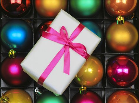 Gift wrapped with white paper and pink bow on multicolor Christmas balls