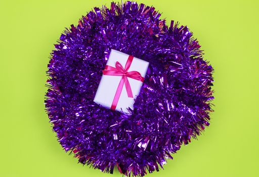 Gift wrapped with white paper and pink bow on purple tinsel on green background