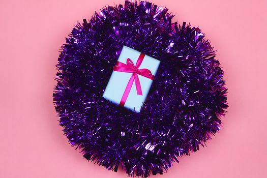 Gift wrapped with white paper and pink bow on purple tinsel on pink background