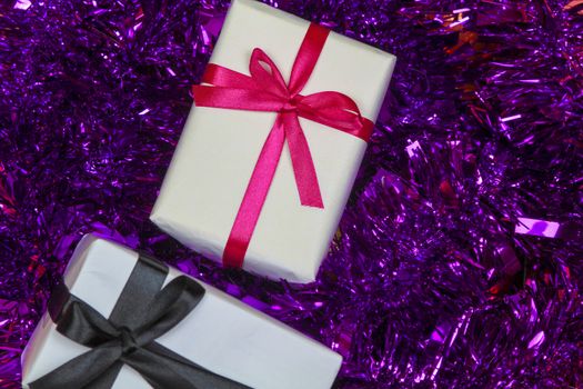 Gifts wrapped with white paper and pink and black bows on purple tinsel