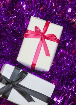 Gifts wrapped with white paper and pink and black bows on purple tinsel