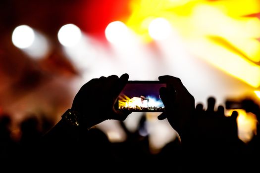 Silhouette of hands using camera phone to take pictures and videos at live concert.