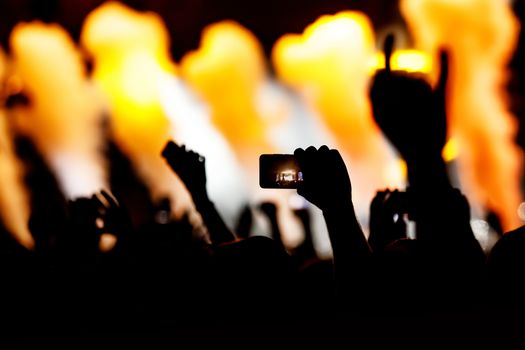 Silhouette of hands using camera phone to take pictures and videos at live concert.