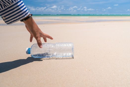 Hand pick up empty water bottle or trash at beautiful beach. Environment Global warming issue.  