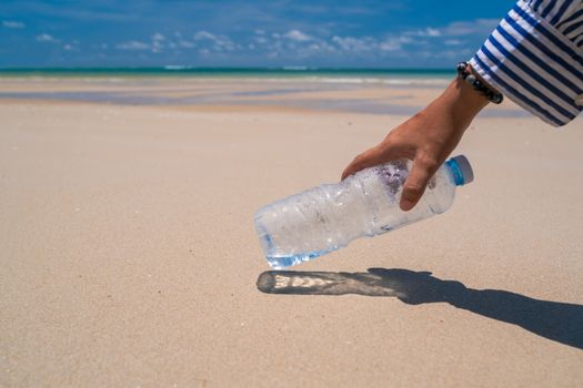 Hand pick up empty water bottle or trash at beautiful beach. Environment Global warming issue.  