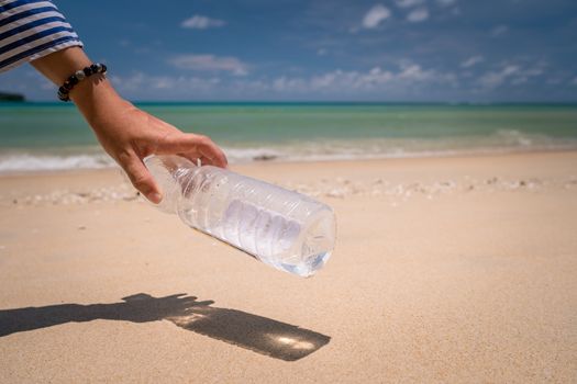 Hand pick up empty water bottle or trash at beautiful beach. Environment Global warming issue.  