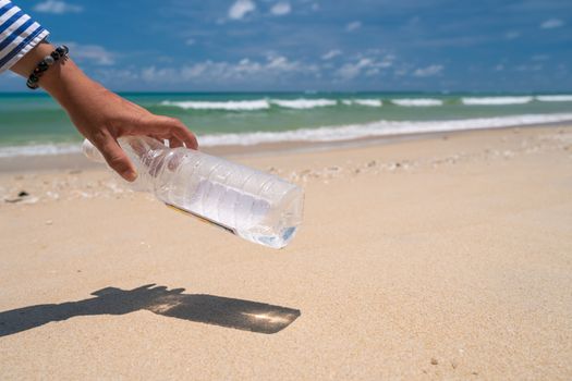 Hand pick up empty water bottle or trash at beautiful beach. Environment Global warming issue.  