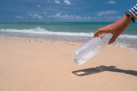 Hand pick up empty water bottle or trash at beautiful beach. Environment Global warming issue.  