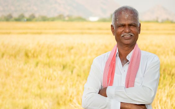 Portrait of Confident smiling Indian farmer with arms crossed standing in front of agriculture farmland looking camera with copy space