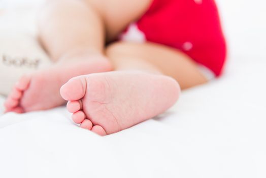 Portrait of beautiful Asian newborn little baby sleeping on white bed at home, Happy baby wears a red shirt relaxing pillow in the room, Family morning at home, close foot