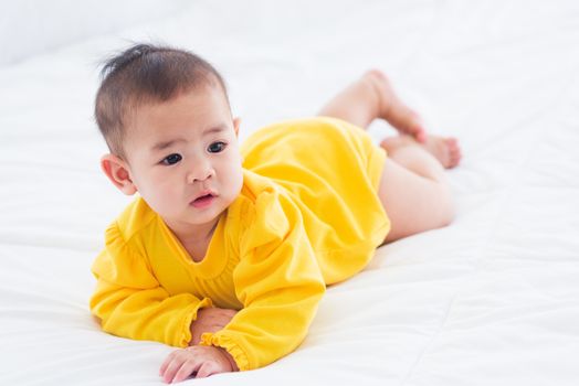 Portrait of beautiful young Asian newborn little baby prone on the bed at home, Happy baby smile wears a yellow shirt relaxing in the room, Family morning at home