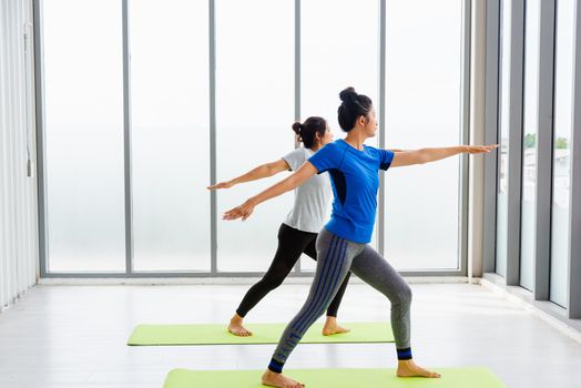 Two Asian women sporty attractive people practicing yoga lesson together, working out at the fitness GYM, Young and senior female exercising do yoga in yoga classes, sport healthy lifestyle