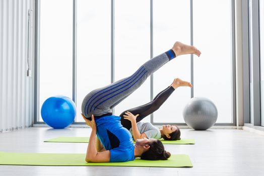 Two Asian women sporty attractive people practicing yoga lesson together, working out at the fitness GYM, Young and senior female exercising do yoga in yoga classes, sport healthy lifestyle