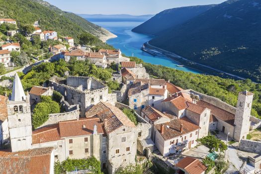 an aerial view of Plomin and Parish Church of the Blessed Virgin Mary with a bell tower, in background Plomin channel, Istria, Croatia