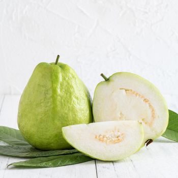 Delicious beautiful guava set with fresh leaves isolated on bright white wooden table background, close up.