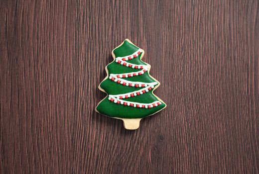 Top view of decorated green plain flavor gingerbread Christmas tree cookie on wooden table background with copy space, concept of holiday celebration.