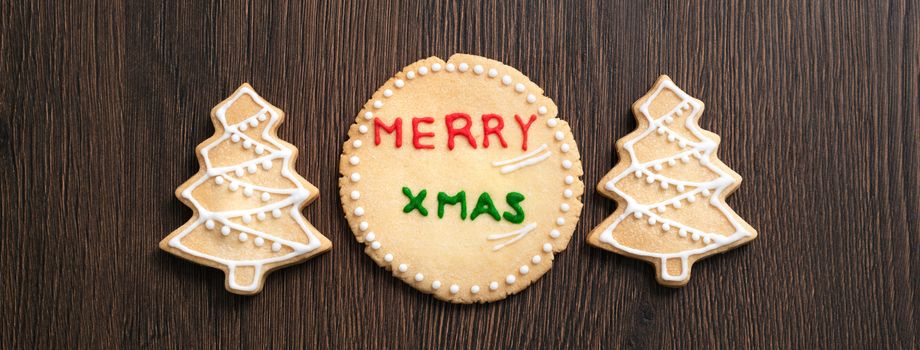 Top view of decorated green plain flavor gingerbread Christmas tree cookie on wooden table background with copy space, concept of holiday celebration.
