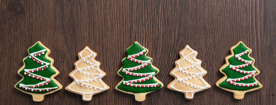 Top view of decorated green plain flavor gingerbread Christmas tree cookie on wooden table background with copy space, concept of holiday celebration.