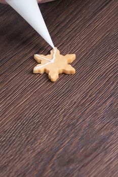Close up of drawing gingerbread Christmas snowflake sugar cookie on wooden table background with white icing, concept of holiday celebration.