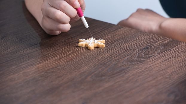 Close up of drawing gingerbread Christmas snowflake sugar cookie on wooden table background with white icing, concept of holiday celebration.