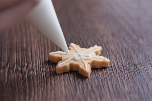 Close up of drawing gingerbread Christmas snowflake sugar cookie on wooden table background with white icing, concept of holiday celebration.