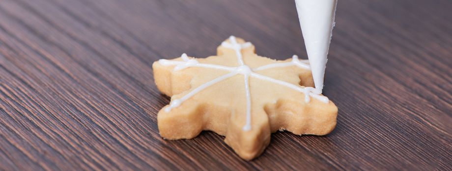 Close up of drawing gingerbread Christmas snowflake sugar cookie on wooden table background with white icing, concept of holiday celebration.